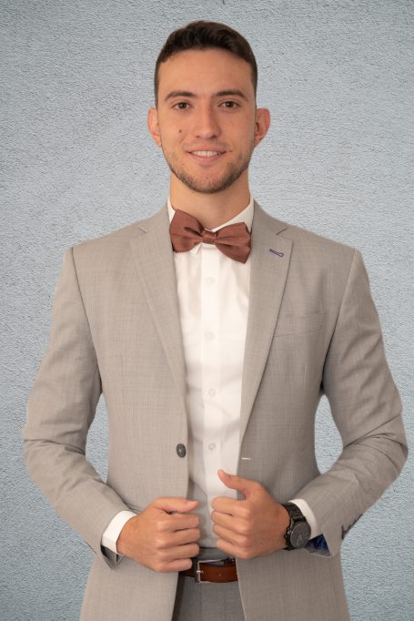 Headshot of a young man dressed in a gray suit and brown bow tie at studio in Miami posing with professionalism.