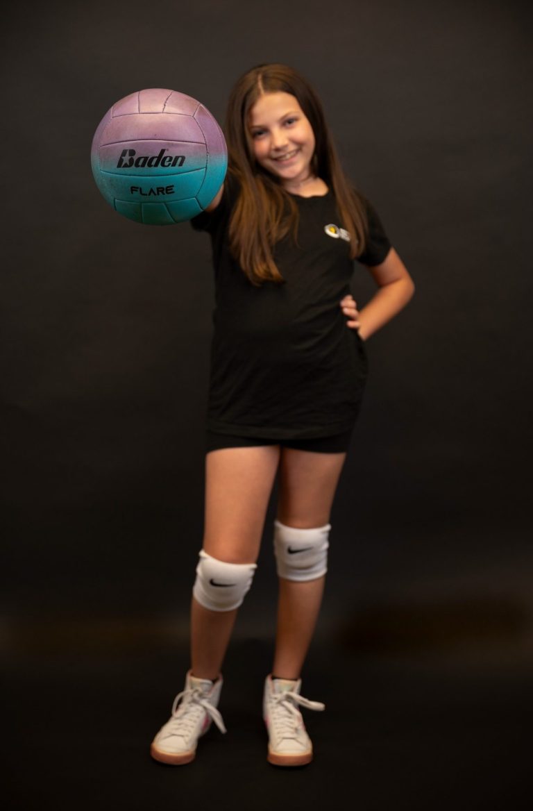 Volleyball athlete at Headshot Studio Portraits posing in a black shirt and white knee pads holding a colorful volleyball