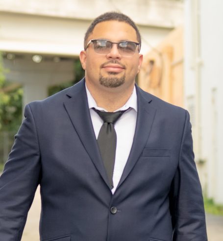 A professional man headshot taken in studio at Headshot Studio Portraits with a suit and sunglasses walking confidently down an urban path.
