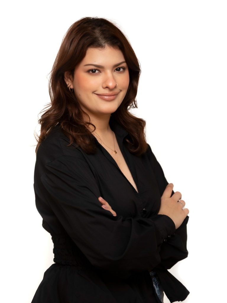 Executive woman with long, wavy hair wearing a dark blue top, smiling against a black background at Headshot Studio Portraits